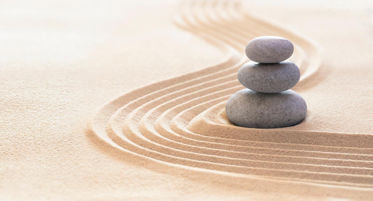 Zen-Garten mit Linien im Sand und gestapelten schwarzen sowie einem hellen Stein
