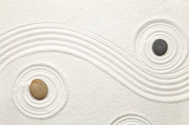Zwei Steine im weißen Sand mit geschwungenen Linien und konzentrischen Kreisen