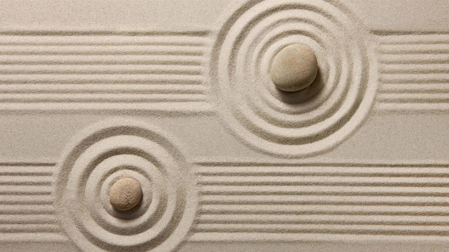 Zwei Steine in feinem Sand mit konzentrischen Kreisen und parallelen Linien