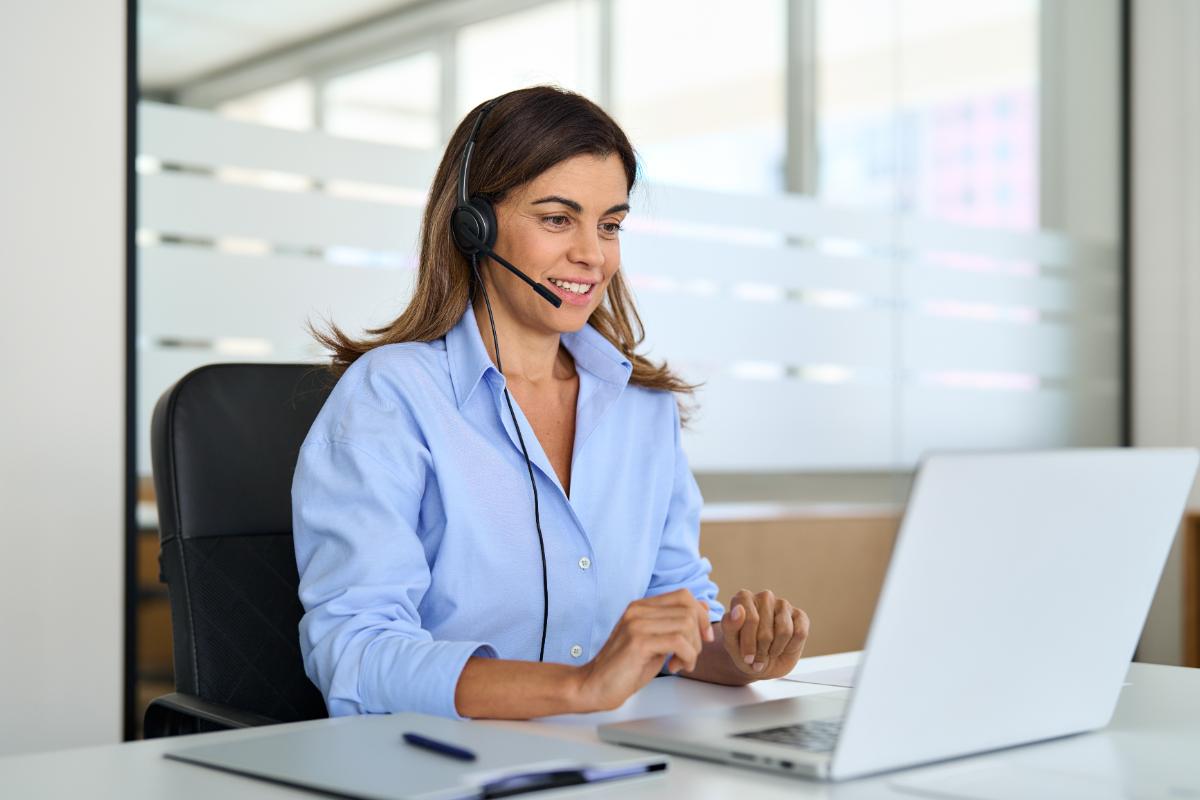 Frau mit Headset arbeitet lächelnd am Laptop in einem modernen Büro